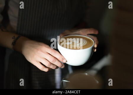 Café barista, latte art holding Coffee Cup, pas de visage ou à la tête, juste les mains montrant et belles illustrations de verser du lait. tatouage au poignet Banque D'Images