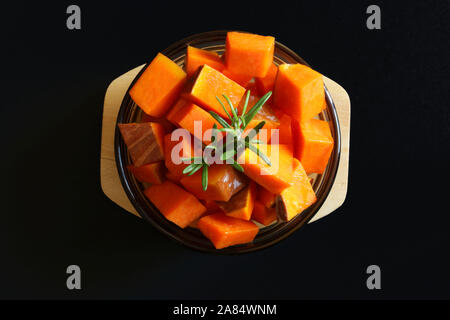 Vue de dessus de morceaux de potiron avec le romarin dans une plaque de verre ronde sur fond sombre. Des légumes crus. Banque D'Images