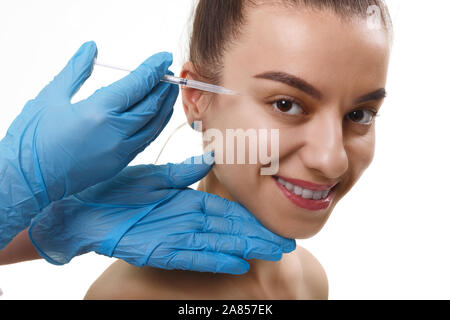 La beauté du visage injections. Portrait belle jeune femme recevant l'injection d'acide hyaluronique. Closeup Of Hands Holding Gants en seringue à proximité Banque D'Images