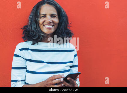 Portrait souriant, woman using smart phone contre fond rouge Banque D'Images