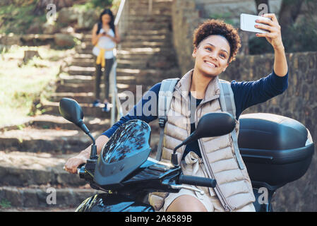 Jeune femme en tenant avec selfies téléphone appareil photo sur scooter Banque D'Images