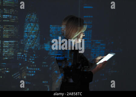 Double exposition businesswoman using digital tablet contre highrise des lumières dans la nuit