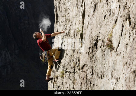 Male rock climber scaling rock face, jusqu'à la craie sur les mains et en soufflant Banque D'Images