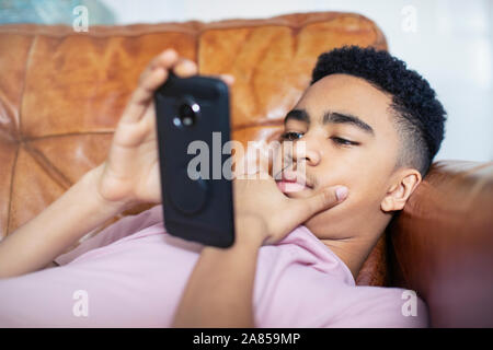 Teenage boy using smart phone on sofa Banque D'Images