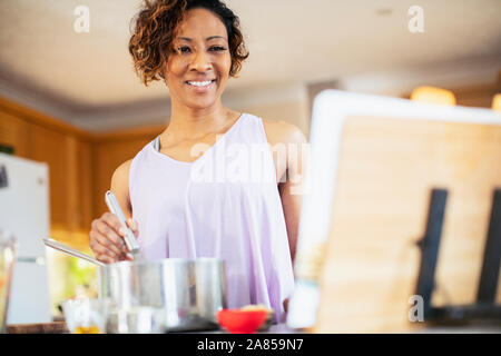 Femme souriante avec cookbook cooking in kitchen Banque D'Images