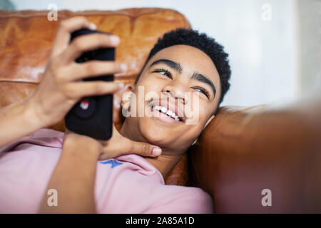 Smiling teenage boy using smart phone on sofa Banque D'Images