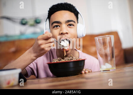 Portrait teenage boy with headphones eating at table Banque D'Images