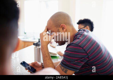 Man with head in hands using smart phone Banque D'Images