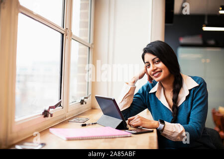 Confiant, Portrait smiling businesswoman using digital tablet in window Banque D'Images