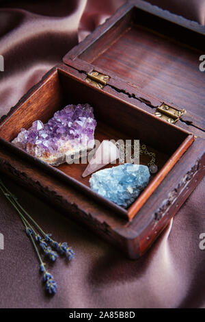 Sorcière outils à l'intérieur belle ancienne boîte en bois. Pendule à quartz rose, amas de cristaux d'améthyste naturel et de célestite. Fleurs de lavande sèches sur violet foncé Banque D'Images