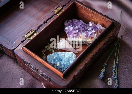 Sorcière outils à l'intérieur belle ancienne boîte en bois. Pendule à quartz rose, amas de cristaux d'améthyste naturel et de célestite. Fleurs de lavande sèches sur violet foncé Banque D'Images