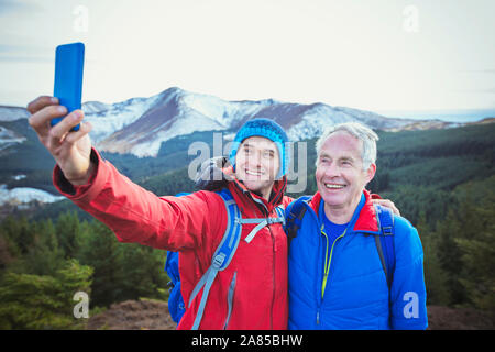 Père et fils de la randonnée, en tenant avec selfies montagnes en arrière-plan, Lake District, UK Banque D'Images