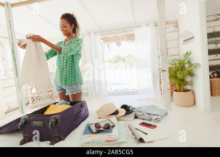 Young woman unpacking suitcase on beach hut bed Banque D'Images