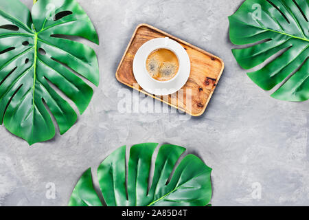 Arrière-plan de béton gris avec plateau en bois et espresso entouré de feuilles tropicales. Mise à plat, vue du dessus. Concept Spa. Banque D'Images