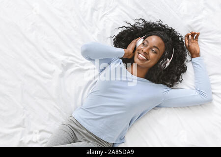 Smiling black girl laying on bed, l'écoute de musique Banque D'Images