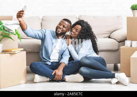 Couple heureux déménagement dans appartement neuf, en tenant le téléphone en selfies Banque D'Images