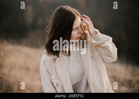 Belle femme assise sur le doux de l'herbe sèche pendant le coucher du soleil. Banque D'Images