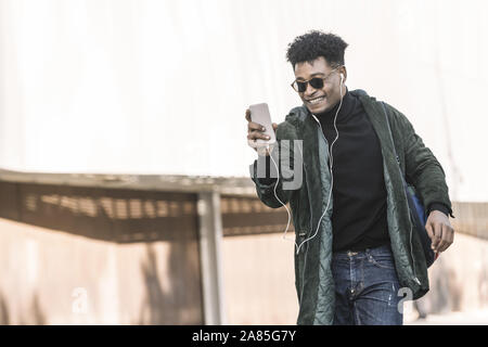 Jeune homme noir avec des écouteurs un appel vidéo avec un téléphone mobile, de la technologie et le mode de vie à l'aide d'internet concept appareil électronique en plein air Banque D'Images