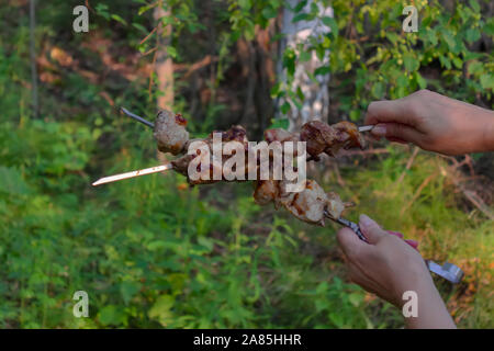 Les mains tiennent une brochette avec des tranches de viande préparé sur le feu. Banque D'Images