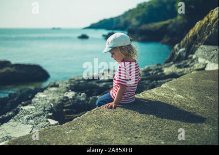 Un petit enfant est assis sur un rocher au bord de la mer Banque D'Images