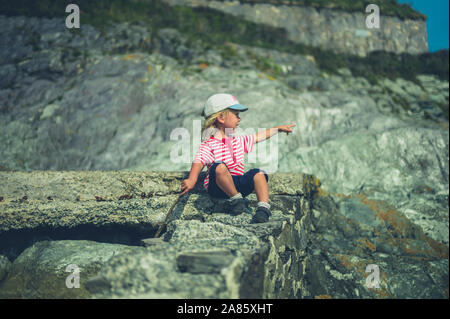 Un petit enfant est assis sur un rocher au bord de la mer Banque D'Images