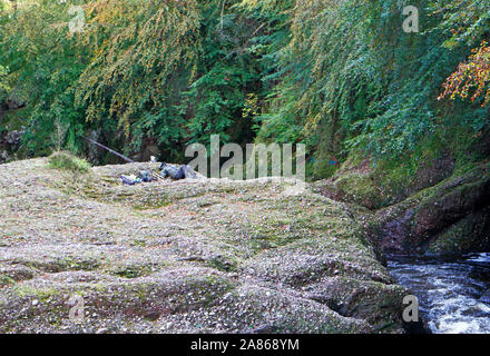 Un pêcheur à la pêche du saumon se reposant sur les rochers de la rivière North Esk près de Conakry, Angus, Scotland, Royaume-Uni, Europe. Banque D'Images