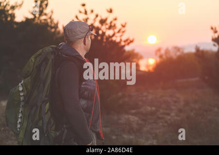 Homme mature avec sac à dos en cap regarder le coucher du soleil à forest Banque D'Images
