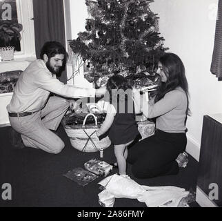 Années 1970, historique, Noël, Angleterre, Royaume-Uni. Cadeaux d'ouverture, mère et père avec jeune fille. Banque D'Images