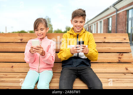 Les enfants avec les smartphones assis sur banc de la rue Banque D'Images