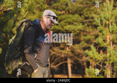 Un homme d'âge mûr avec un sac à dos vêtements touristiques, lunettes de soleil et un chapeau. Forêt en arrière-plan. Banque D'Images