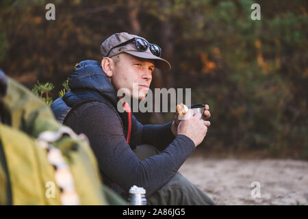 Mature male hiker faisant une pause pour manger et boire tout en faisant de la randonnée en plein air Banque D'Images