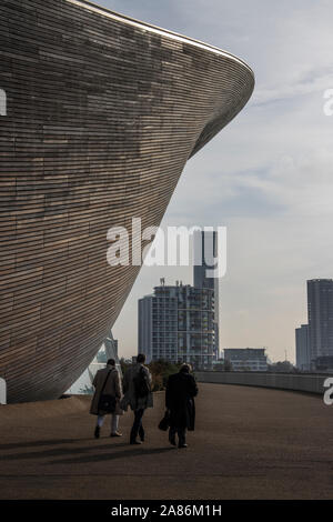 Des hommes en manteaux d'hiver passé l'Aquatics Centre de Londres conçu par Zaha Hadid, au Queen Elizabeth Olympic Park à Stratford, London, England, UK Banque D'Images