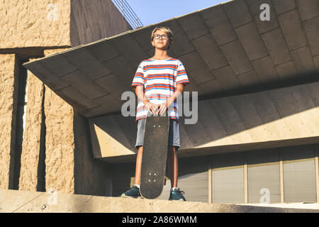 Jeune homme debout du skate park avec ses roulettes dans les mains, à la suite de graves. En attente de l'adolescence Les amis de l'école. 23-08-2003 détente patineur Banque D'Images