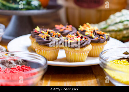 Le thème de l'automne mini cupcakes. Yellow cake au chocolat avec glaçage orange, rouge, jaune et paillettes. Cupcakes sur plaque blanche ronde. Banque D'Images