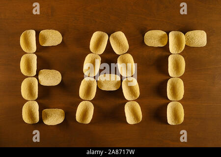 Croustilles de pommes de terre sur une table en bois, l'arrière-plan avec le texte "manger", concept design sur le thème de la restauration rapide, mauvaise alimentation et risque accru d'obésité Banque D'Images