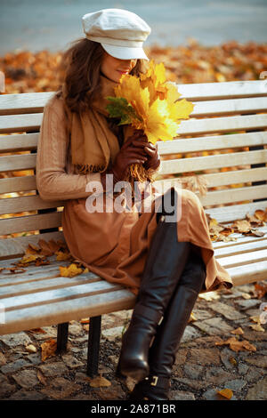 Bonjour l'automne. ambiance trendy femme en pull, jupe, chapeau, gants et écharpe avec feuilles jaunes profitez de l'automne alors qu'il était assis sur un banc à l'extérieur dans l'un Banque D'Images