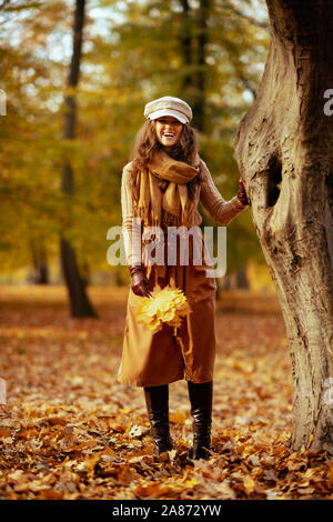 Bonjour l'automne. Portrait de femme à la mode en pull, jupe, chapeau, gants et écharpe avec feuilles jaunes à l'extérieur dans le parc de l'automne. Banque D'Images