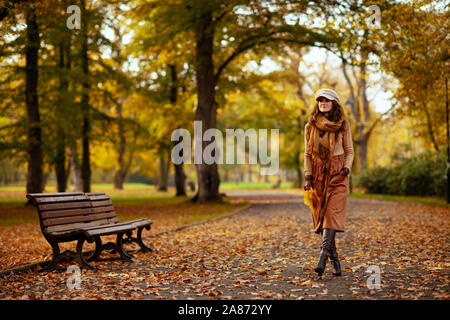 Bonjour l'automne. Portrait de femme à la mode heureux en pull, jupe, chapeau, gants et écharpe avec feuilles jaunes la marche à l'extérieur à l'automne pa Banque D'Images