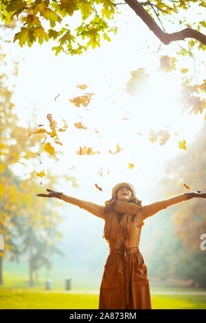 Bonjour l'automne. Heureux femme élégante en pull, jupe, chapeau, gants et écharpe en plein air dans le parc automne bénéficiant d'automne et attraper la chute lea jaune Banque D'Images