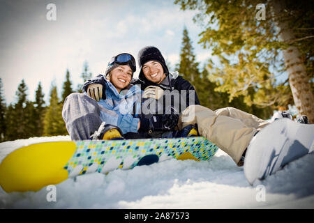 Portrait of a smiling woman wearing ski gear et assis avec leurs planches à l'extérieur dans la neige. Banque D'Images