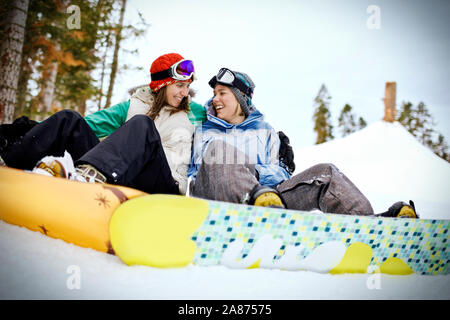 Deux jeunes femmes souriant assis à côté de l'autre tout en restant fixé à snowboards et assis dans la neige. Banque D'Images