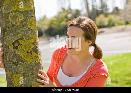 Teenage girl peeking sur le côté d'un arbre. Banque D'Images