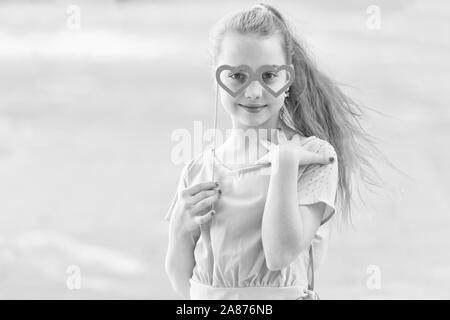 Valentines adorable fille. Cute kid holding fancy Valentines Day party props sur stick. Petit enfant regardant à travers des lunettes en forme de coeur le Jour de Valentines. Happy valentines day, copiez l'espace. Banque D'Images