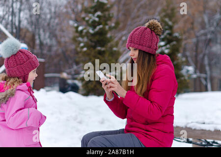 Créer du contenu à l'aide de photo pour smartphone blog familial sur le réseau social. Habillés avec élégance la mère et la fille sont photographiés sur un pied d'hiver. Happ Banque D'Images