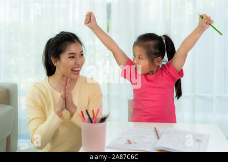 Heureux succès étudiant maternelle asiatique et sa mère les mains levées jusqu'à célébrer la réussite pour faire ses devoirs dans la salle de séjour à la maison. Ar l'enfant Banque D'Images