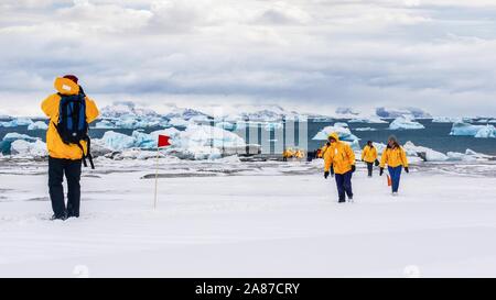 Tourisme en Antarctique, en tant que touristes portant des parkas correspondant à pied sur la neige, avec vue sur la mer et les icebergs dans l'arrière-plan. Banque D'Images