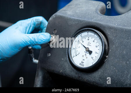 Close-up Un atelier travailleur dans les gants de appuie sur un bouton d'un pneu de voiture avec changeur d'un capteur de pression du volant. Travailler à l'atelier de pneus Banque D'Images