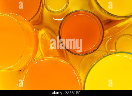 Composition abstraite Vue de dessus du jus d'orange et jaune en forme de boissons diverses lunettes avec des tranches de fruits orange et placés sur fond jaune Banque D'Images