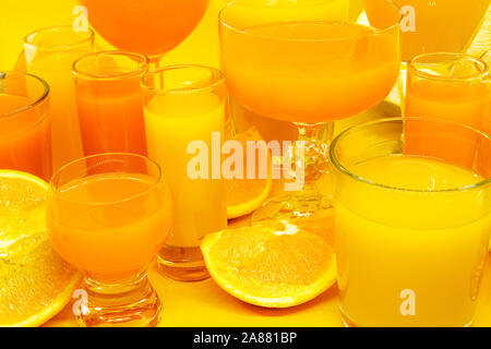Composition abstraite de jus d'orange et de jaune en forme de boissons diverses lunettes avec des tranches de fruits orange et placés sur fond jaune avec l'exemplaire Banque D'Images