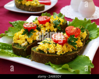 Des sandwichs avec des oeufs brouillés et tomates cerises sur du pain avec des orties Banque D'Images